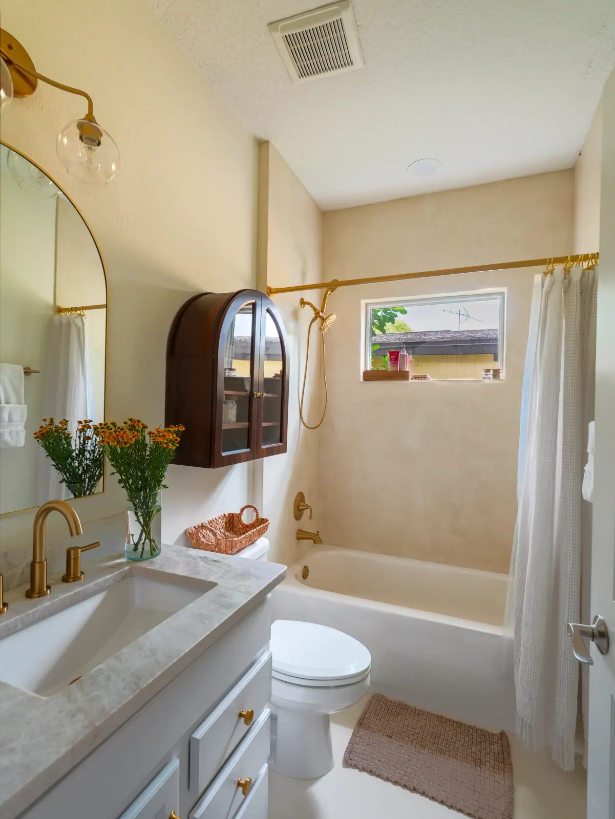 Arched walnut wall cabinet beside a microcement tub surround