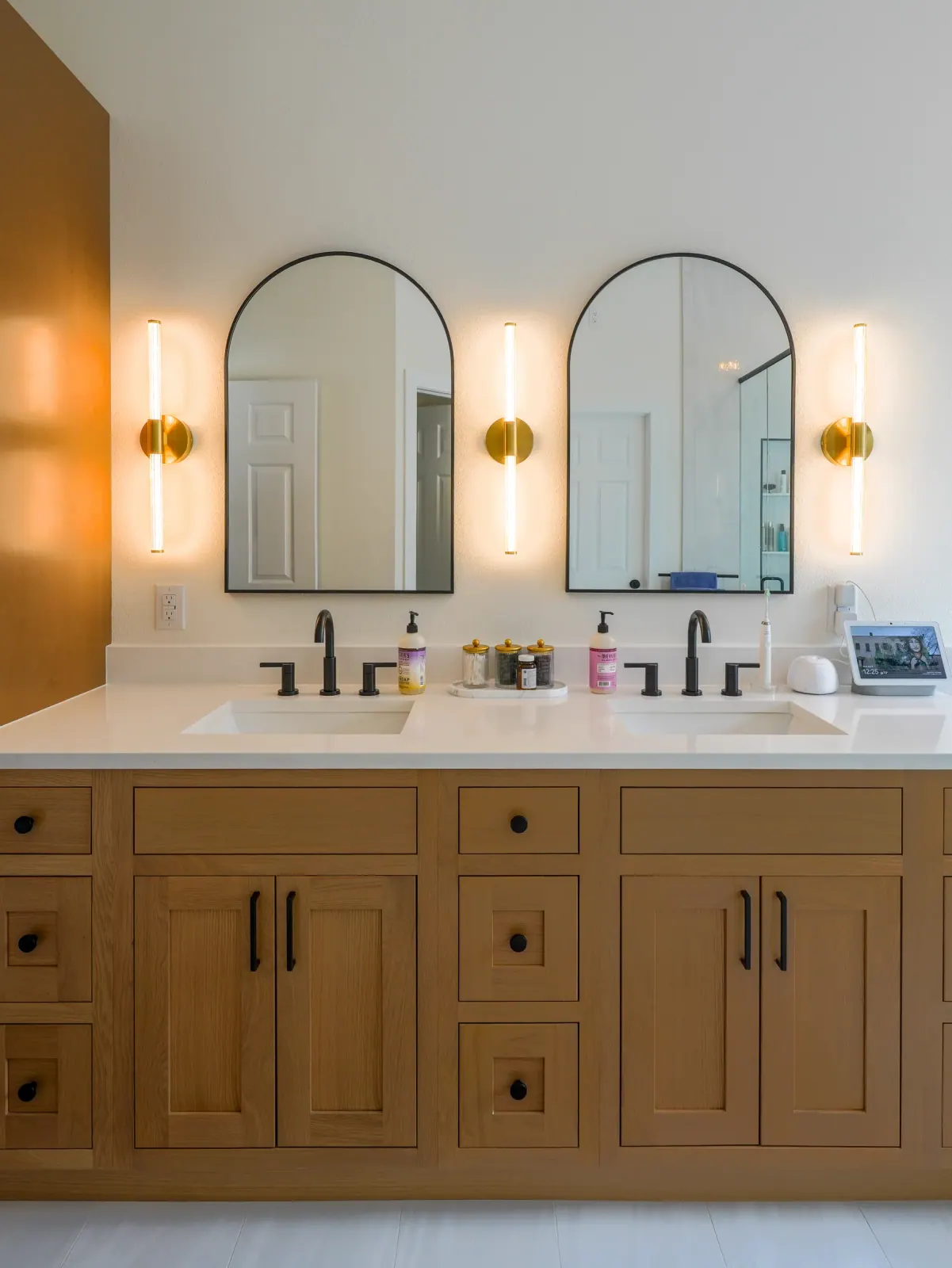 Oak double vanity with arched mirrors and brass sconces