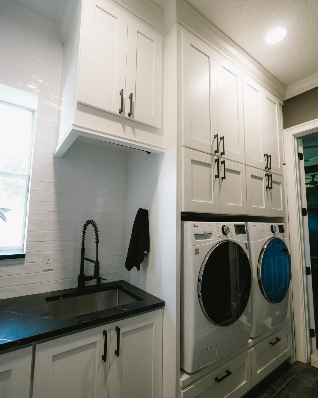 Laundry room with white cabinets and a black counter