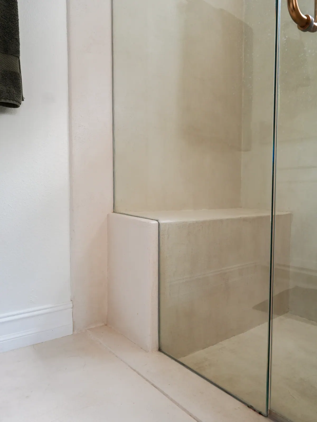 Walk-in shower with a seamless microcement bench and glass panel