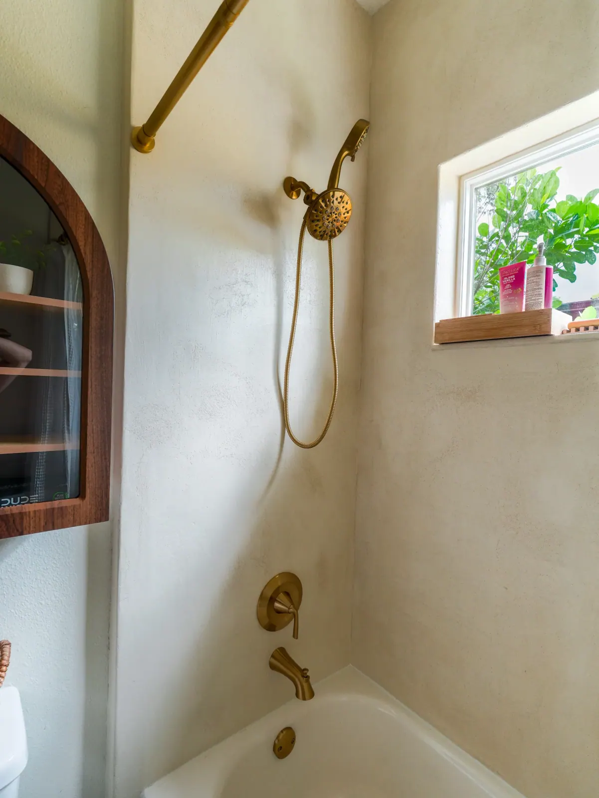 Microcement shower wall with a brass handheld shower and a window